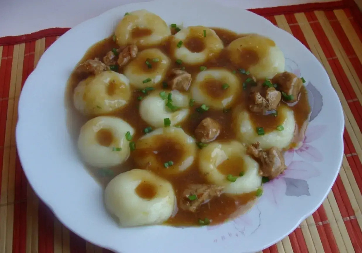 Kluski śląskie z gulaszem, polane sosem i posypane szczypiorkiem. Pyszny sposób, jak zrobić kluski śląskie.